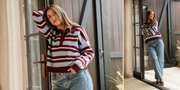 Woman wearing a striped sweater and jeans standing in front of a glass door.