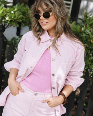 Woman wearing a pink jacket over a pink shirt with sunglasses, standing outdoors.