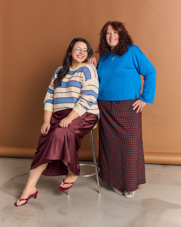 Two women posing together against a brown background