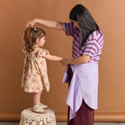 Woman helping a young girl stand on a stool against a brown background