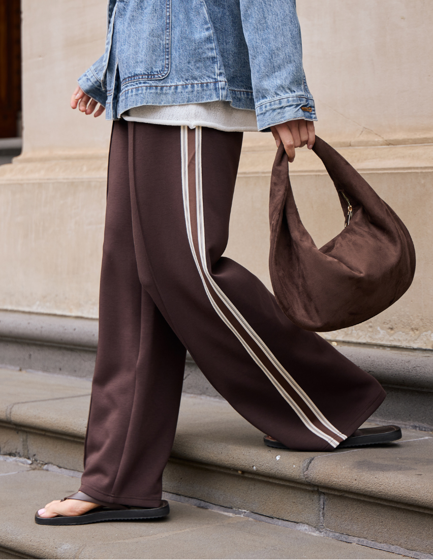 Person wearing brown pants with white stripes, holding a brown bag, standing on steps.